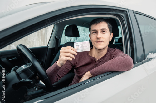 Caucasian man shows his driver's license in the car window immediately after passing the exam or at the request of the traffic police