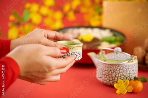 Hands of woman drinking cup of green tea with sweet driend fruits at Chinese New Year celebration