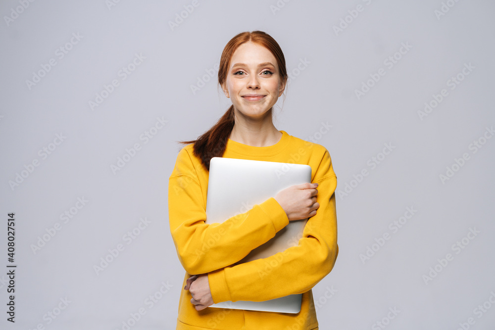 Charming young woman student holding laptop computer and looking at camera on isolated white background. Pretty lady model with red hair emotionally showing facial expressions in studio, copy space. Charming young woman student holding laptop computer and looking at camera on isolated white background. Pretty lady model with red hair emotionally showing facial expressions in studio, copy space.