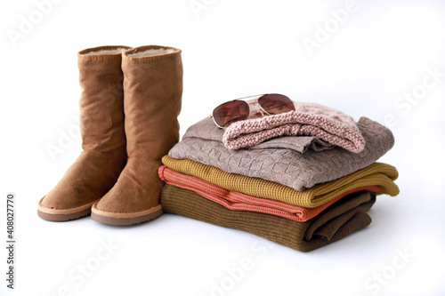 Stack of cozy knitted sweaters and winter boots on white background. Autumn-winter concept.