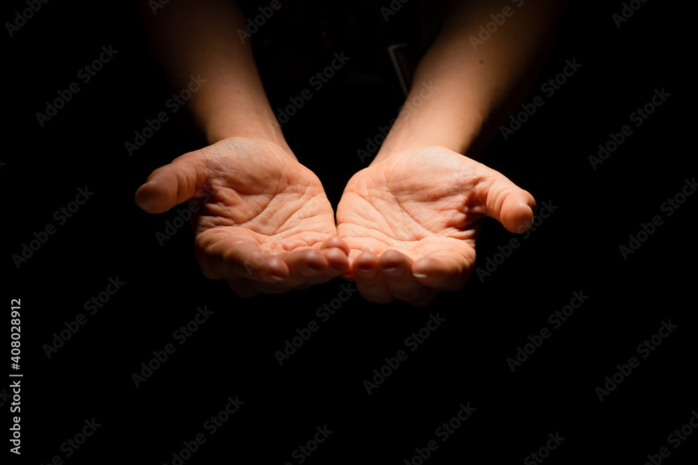 Two hands with open palms turned up, offering or giving something, a handful. Hands on a black background, contrasting dramatic light from above Two hands with open palms turned up, offering or giving something, a handful. Hands on a black background, contrasting dramatic light from above