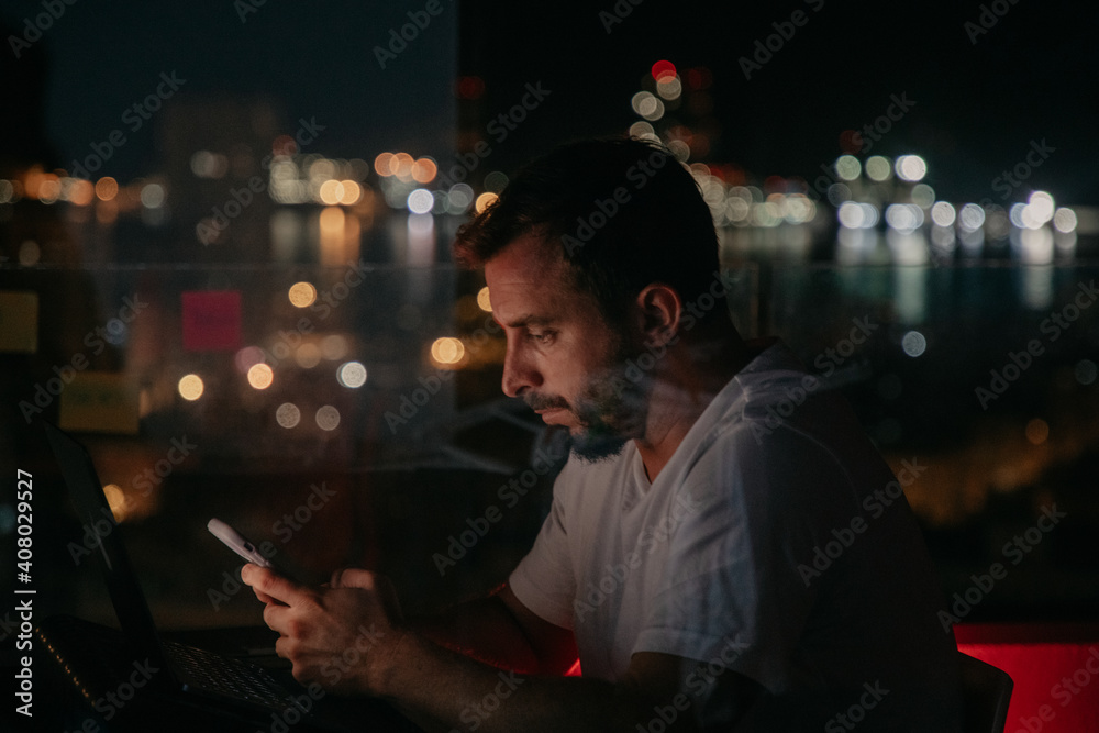 young man working in front of the computer and mobile phone at night while writing messages and working on the city young man working in front of the computer and mobile phone at night while writing messages and working on the city