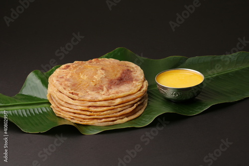Puran Poli, also known as Holige, is an Indian sweet flatbread from India consumed mostly during Holi festival. Served on banana leaf with pure Ghee over black background.