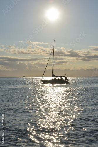 Silhouette of yacht with people crossing sun reflection in sea water, sun shining above. Expedition to the Kuril islands to the south from Kamchatka peninsula.