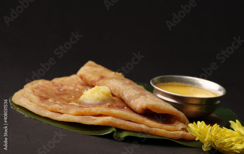 Puran Poli, also known as Holige, is an Indian sweet flatbread from India consumed mostly during Holi festival. Served on banana leaf with pure Ghee over black background.