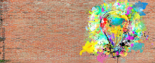 Big stylized light bulb on a big wall of bricks drawn with splashes of colored paint. Concept of innovation and creativity brick