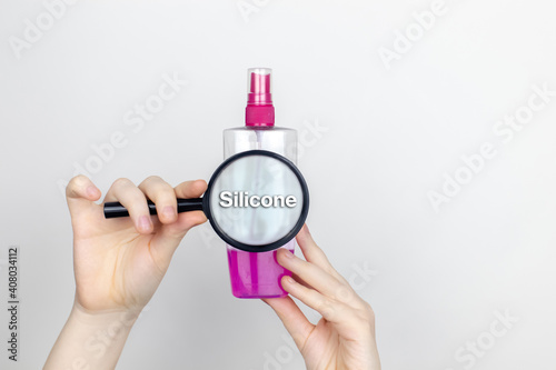 A woman examines the harmful ingredients of the hair spray a magnifying glass. Means with Silicone. The concept of hazardous substances in cosmetics and household chemicals photo