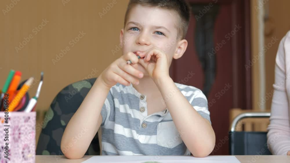 Young mother sitting at a table at home helping her son with his homework from school Young mother sitting at a table at home helping her son with his homework from school