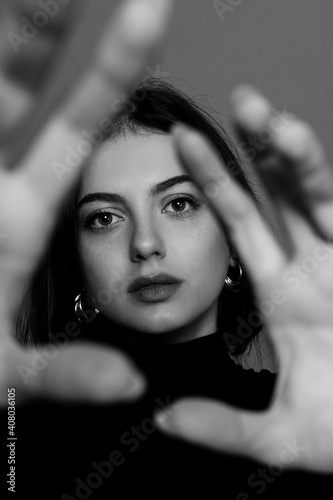 Dramatic black and white portrait of young woman looking through her hands