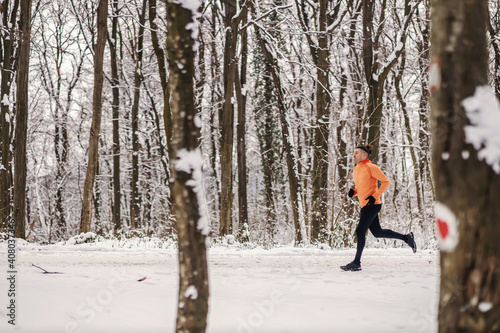 Fast sportsman jogging in forest on snowy winter day. Healthy lifestyle, winter fitness