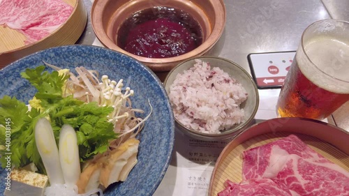 Japanese Sukiyaki hot pot with raw egg, sliced beef meat,tofu curdled soy milk, negi welsh onion,shungiku crown daisy,gobou greater burdock,shirataki konjac,fu wheat gluten,enoki mushrooms and rice. photo