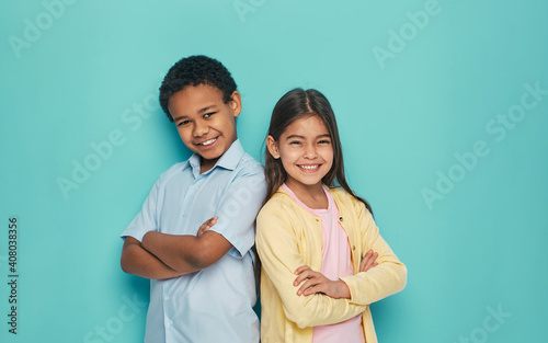Asian girl and African American boy standing back to back with arms crossed on a turquoise background