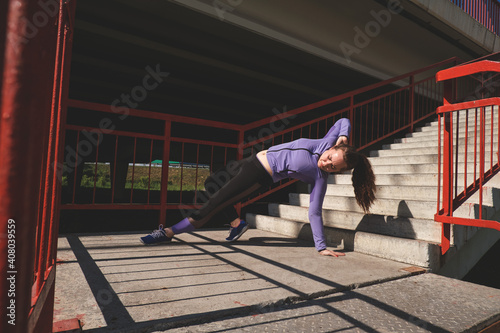 Young woman stands on one hand doing a workout. Active lifestyle concept.