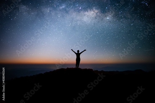 Silhouette of young traveler watched the star and milky way on top of the mountain alone before sunrise. He raised his arms over his head, expressing his joy and success, and enjoyed his hike.