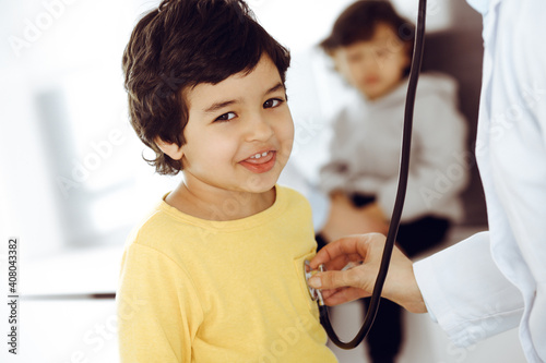 Woman-doctor examining a child patient by stethoscope. Cute arab boy at physician appointment. Medicine help concept