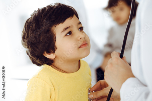 Woman-doctor examining a child patient by stethoscope. Cute arab boy at physician appointment. Medicine help concept