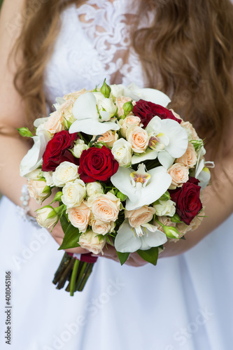 Wedding bouquet of roses and orchids in the hands of the bride