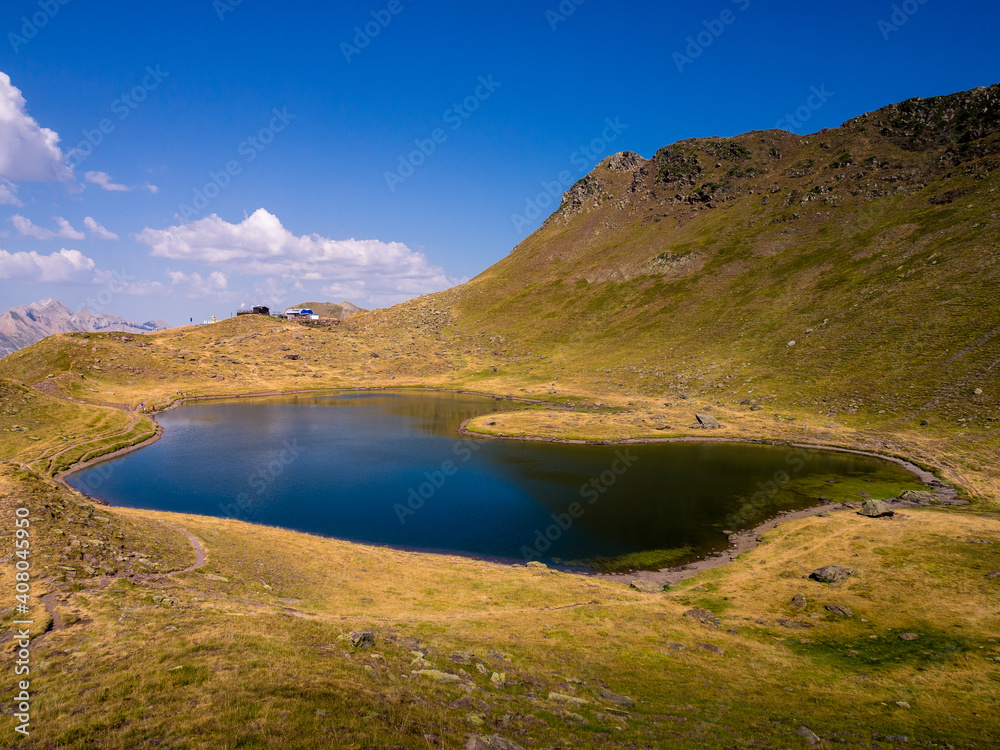 Lago de alta montaña rodeado de montañas y praderas verdes en un dia de cielo azul en verano en Pirineos