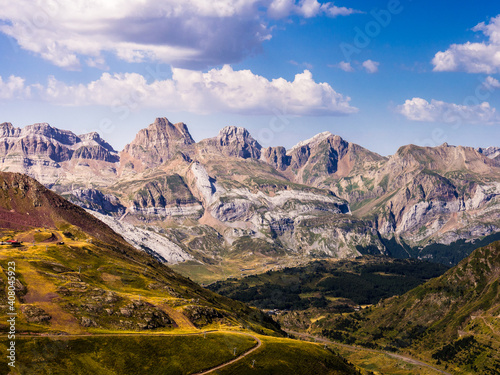 Montañas de los Pirineos sobre pastos verdes y con cielo azul de nubes blancas
 photo