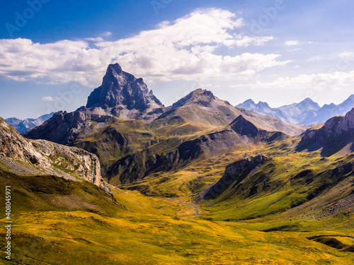 Montaña con forma de piramide destaca sobre el paisaje alpino de los Pirineos y el cielo azul con nubes blancas