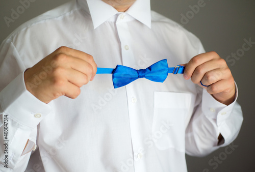 A man in a white shirt holds a bow tie in his hands