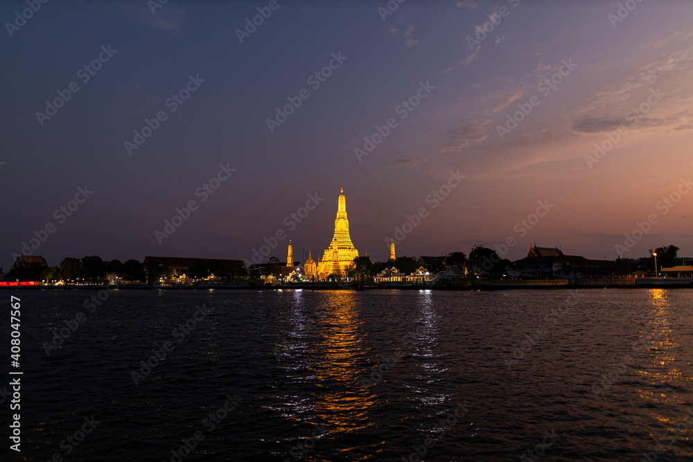 View of Illuminated Wat Arun Temple from the Chao Phraya river in sunset. Buddhist temple in Bangkok, Thailand