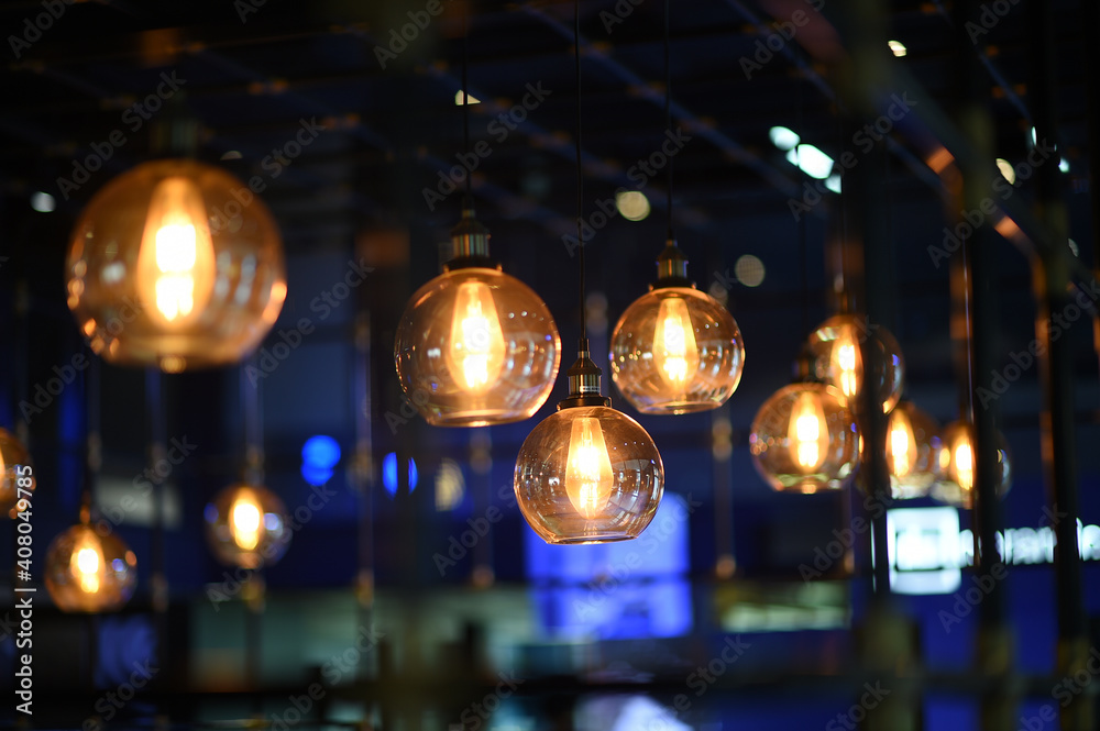 Close up of many modern light gold glass ball hanging lamp with the light on, decorated in the blurred beautiful blue room in a restaurant or coffee shop