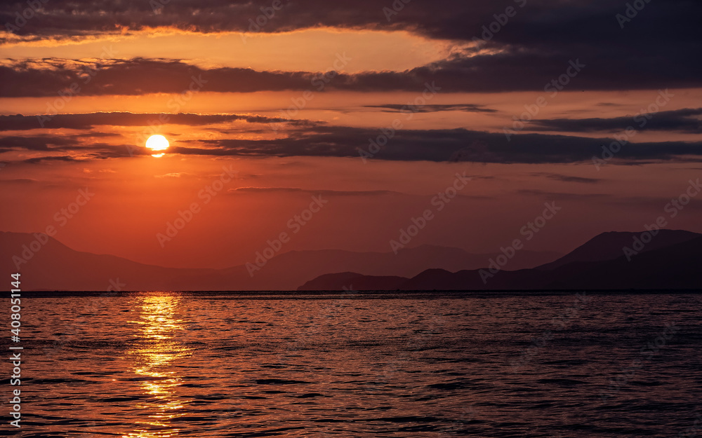 orange fiery sundown sky with some clouds over calm sea, scenic nature background