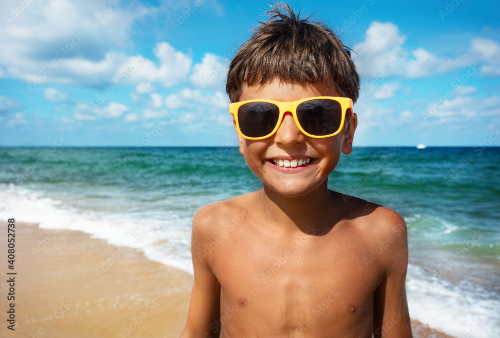 Close happy portrait of the smiling boy in sunglasses with beach on background Close happy portrait of the smiling boy in sunglasses with beach on background