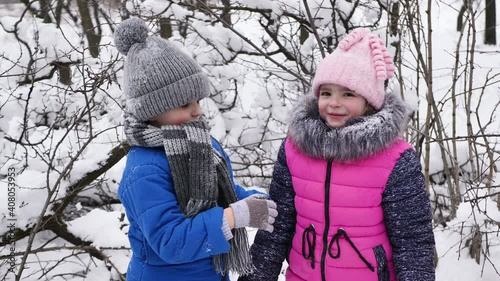 Children, a boy and a girl, hug and kiss in the winter in the cold in the snow-covered forest. photo