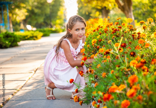 A cute charming girl in a beautiful pink dress sniffs fiery marigolds in a bright park on a sunny day on a long-awaited vacation