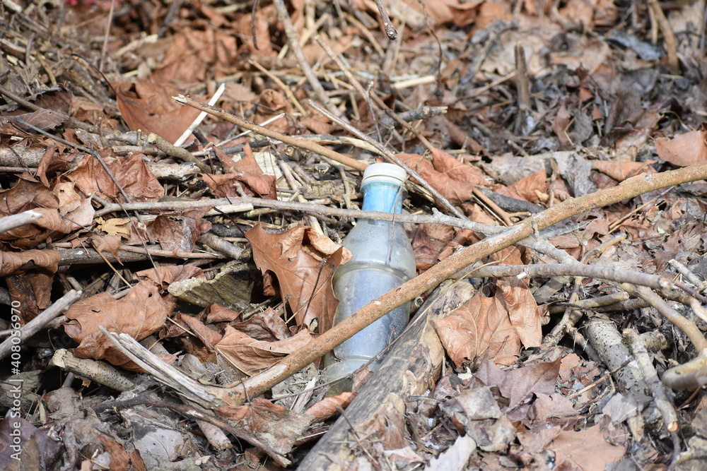 Fototapeta premium Discarded plastic water bottle littering dry creek bed with dried brown leaves and twigs creating environmental pollution