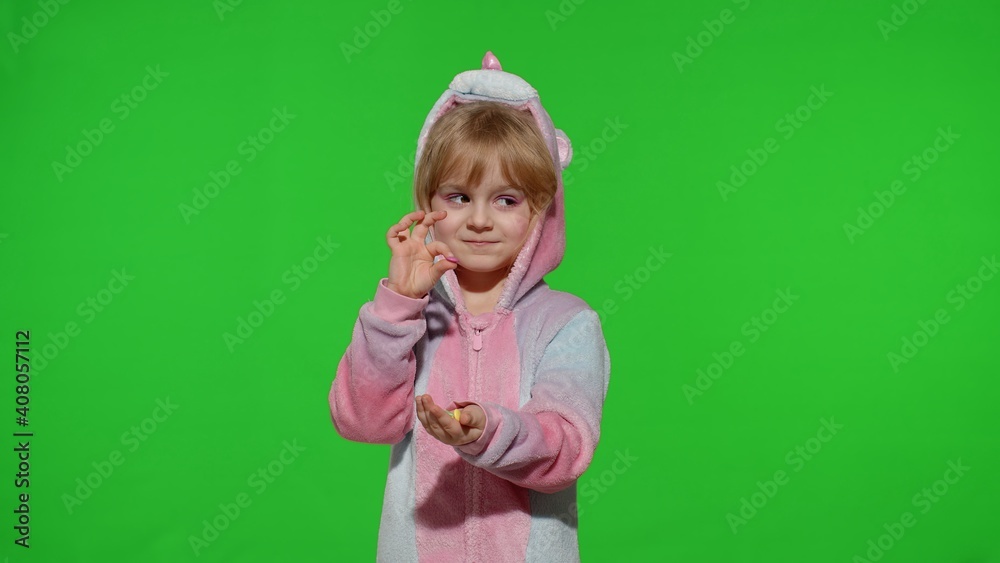 Portrait of a cute little child smiling, enjoying eating sweets candies dessert in unicorn costume on chroma key green background. Model kid girl animator in unicorn pajamas. Copy space Portrait of a cute little child smiling, enjoying eating sweets candies dessert in unicorn costume on chroma key green background. Model kid girl animator in unicorn pajamas. Copy space