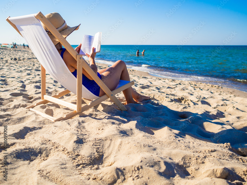 Woman relaxing on beach reading book sitting on sunbed Woman relaxing on beach reading book sitting on sunbed
