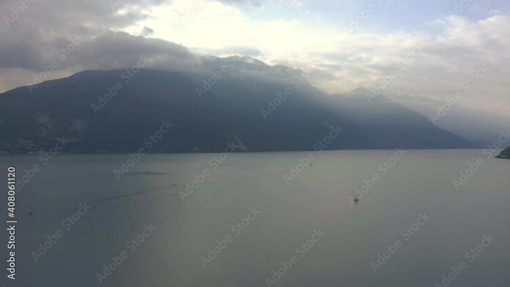 Dolly in aerial shot of Lake Garda with the morning sun breaking through the clouds and spilling light over the majestic mountains Dolly in aerial shot of Lake Garda with the morning sun breaking through the clouds and spilling light over the majestic mountains