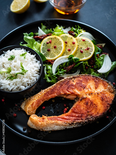 Fried salmon steak with basmati rice and  mix of vegetables served on black plate on wooden table
