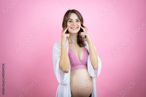 Young beautiful brunette woman pregnant expecting baby over isolated pink background smiling confident showing and pointing with fingers teeth and mouth