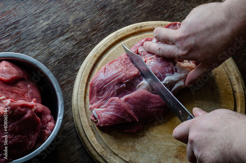 Male hands chop with a knife Large pieces of fresh raw beef on a cutting board.