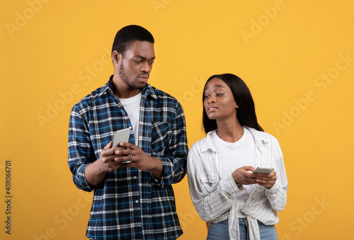 Interested young african american wife peeks in smartphone of displeased husband