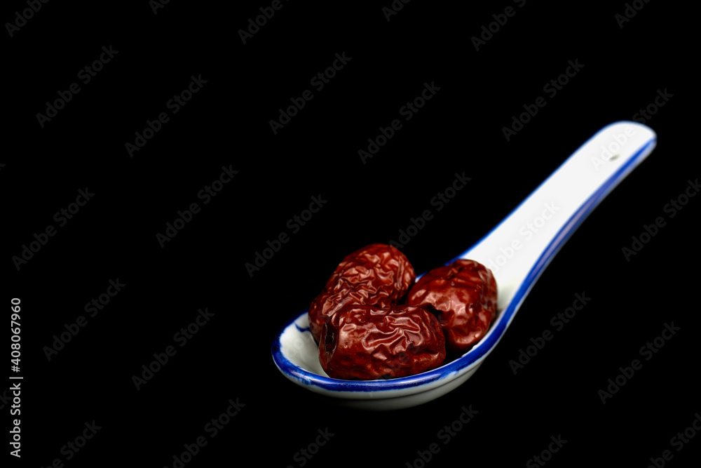 Red Date Jujube on a Ceramic Chinese Soup Spoon isolated on black background. Selective focus.