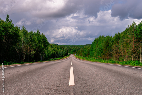 Photos An asphalted intercity road with white markings extending into the distance through a green forest