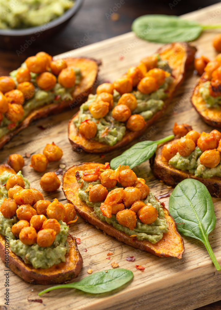 Sweet potato toast loaded with avocado guacamole and baked chickpeas sprinkled with chili flakes served on wooden board
