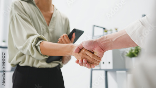 Multiracial group of young creative people in smart casual wear discussing business shaking hands together and smiling while standing in modern office. Partner cooperation, coworker teamwork concept.