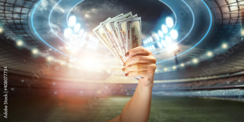 Close-up of a man's hand holding US dollars against the background of the stadium. The concept of sports betting, making a profit from betting, gambling. American football. photo