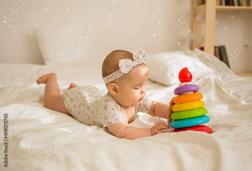 Wallpaper Mural a baby girl lies and plays with a pyramid on a white blanket on a bed with a copy of the space Torontodigital.ca