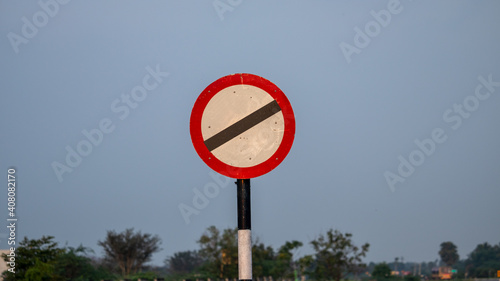 Clear Photo of No entry or Restricted Road Sign board in Circle Shape with white background and thick red border attached to Rusty Pole in Side path of Highways in sky and greenary background