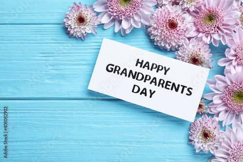 Beautiful flowers and card with phrase Happy Grandparents Day on light blue wooden background, flat lay. Space for text