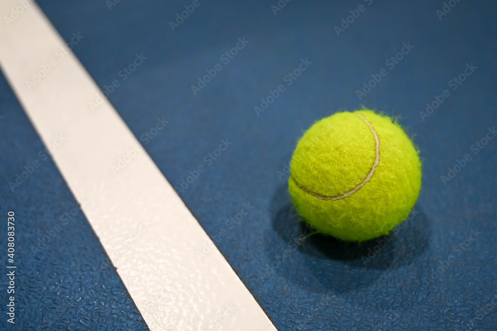 Close-up of tennis ball on blue hard court with white stripe.