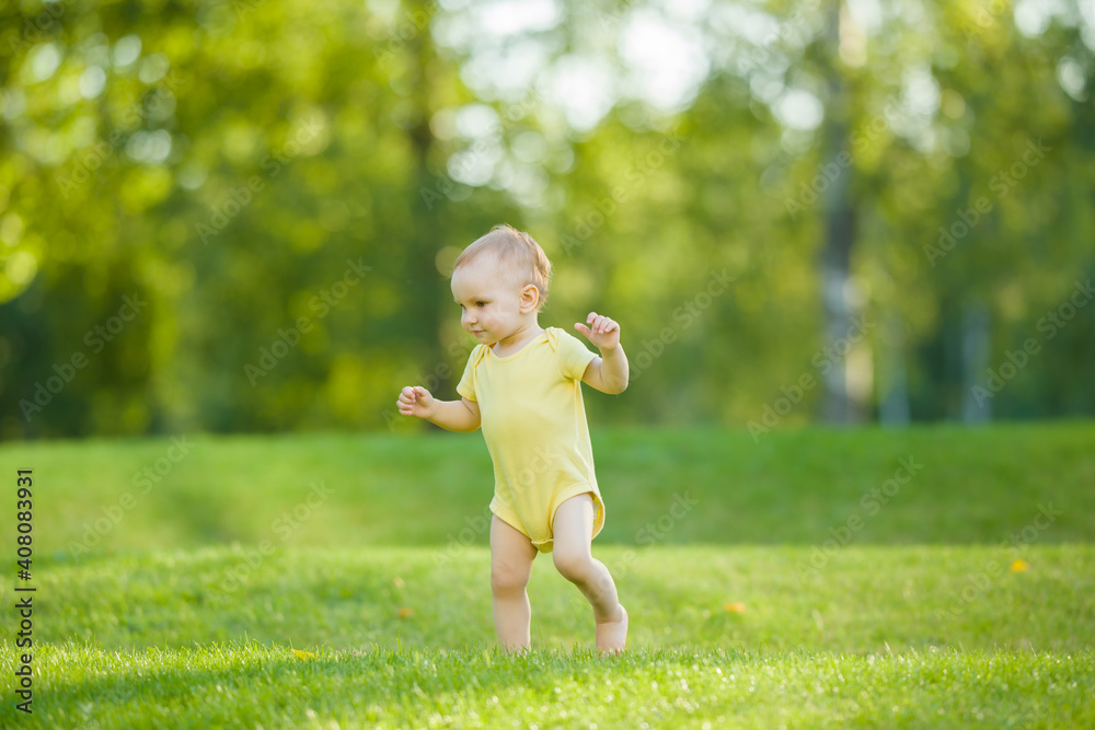 One happy beautiful baby girl in yellow bodysuit running barefoot on fresh green grass in warm sunny summer day. Side view.