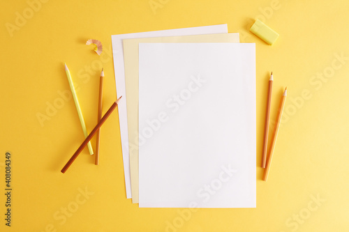 Colorful pencils, eraser and empty white papers . Empty place for text or drawing on the yellow background..
